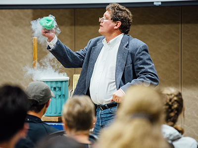A professor holds a beaker in front of a sample class.