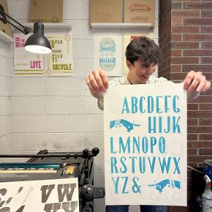 A student holds their letterform type specimen page. 