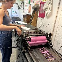 A student is letterpress printing her interior page in pink. 