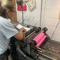 A students uses the press to print the first layer in pink on their interior page. 