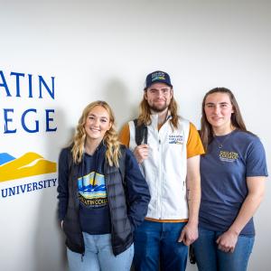 A group of students standing next to a Gallatin College sign