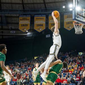 A basketball player reaches for a dunk over an opponent