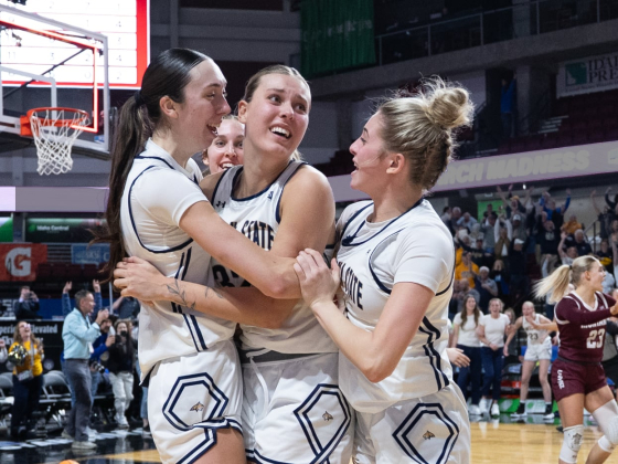 Montana State University women's basketball players celebrate on the court after winning the Big Sky Conference tournament. Three players in white MSU uniforms embrace with joyful expressions, while opposing players in maroon uniforms react nearby. In | MSU Athletics photo