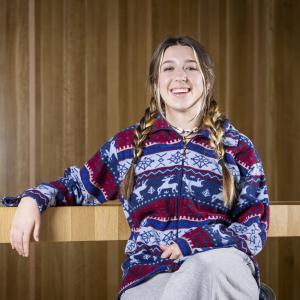 A portrait of Ashlin Ivester sitting in front of a wood wall