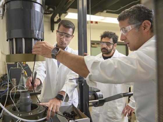 Three men stand around a scientific machine while two of them reach in to adjust something on the machine | MSU Photo by Colter Peterson