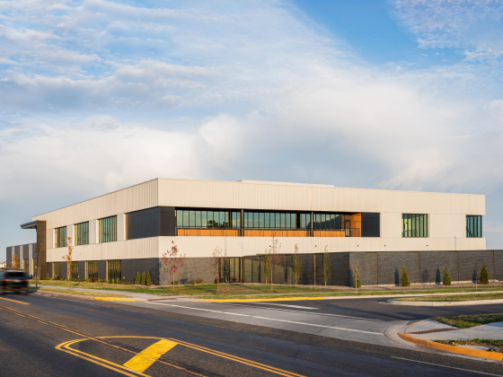 A modern two-story commercial building with a white and gray exterior sits at the corner of an urban street under a blue, partly cloudy sky. Large windows line the upper and lower levels, and the building features clean architectural lines with landscaped | Image courtesy of Aurora