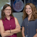 Erica Antill and Alexis McDonnell standing together in a lab with a poster of Mars in the background