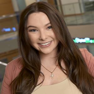 Whitney Vralsted standing in Jabs Hall in front of a stock ticker