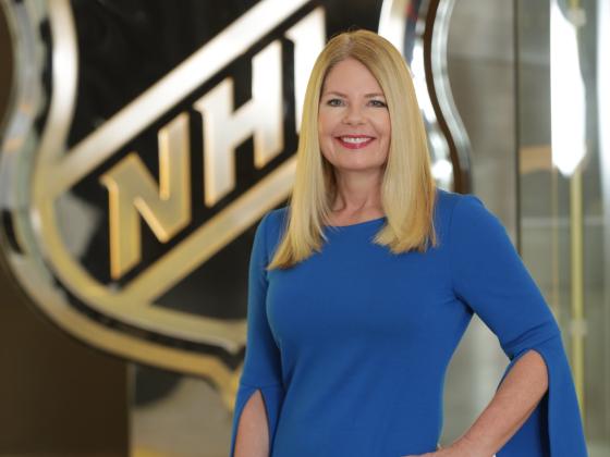 A woman in a blue dress poses in front of the NHL logo.  | 