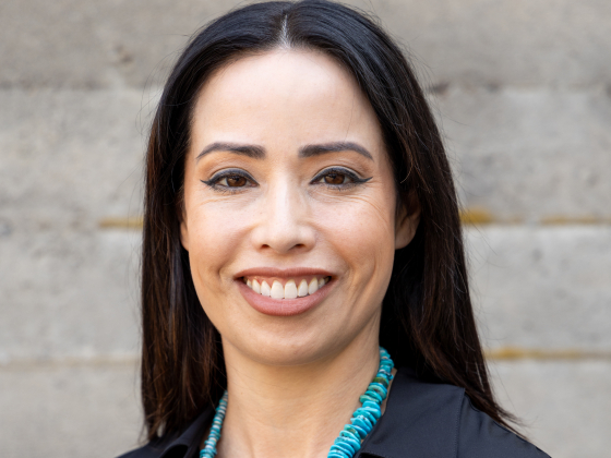 A smiling, dark-haired woman with a turquoise necklace draped around a black shirt. | 