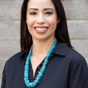 A smiling, dark-haired woman with a turquoise necklace draped around a black shirt.