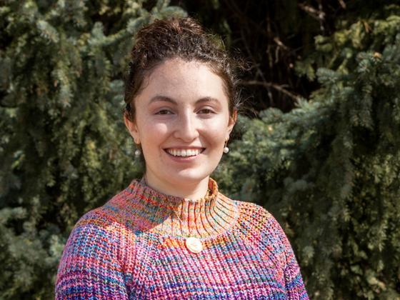 A woman with brown hair and a pink sweater smiles for a photo in front of trees | MSU photo by Marcus "Doc" Cravens