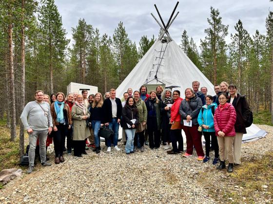 A group of people standing outdoors in front of a tipi | 