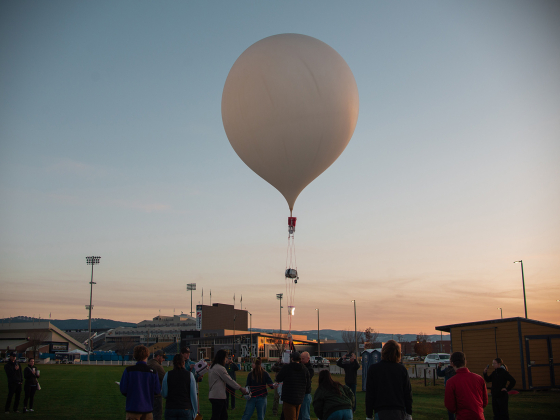 A group of people launching a large balloon with a sunset sky in the background | Photo by Frank Frederick