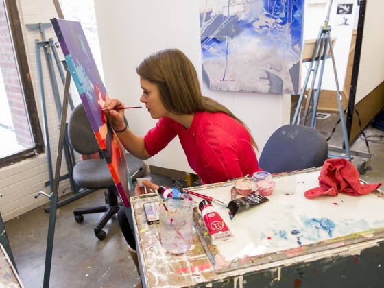 A student paints on an easel | Photo by Kelly Gorham