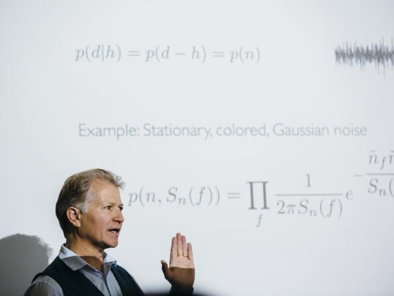 Photo of Neil Cornish standing in front of a screen with equations projected on it. | MSU Photo by Adrian Sanchez-Gonzalez
