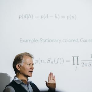 Photo of Neil Cornish standing in front of a screen with equations projected on it.