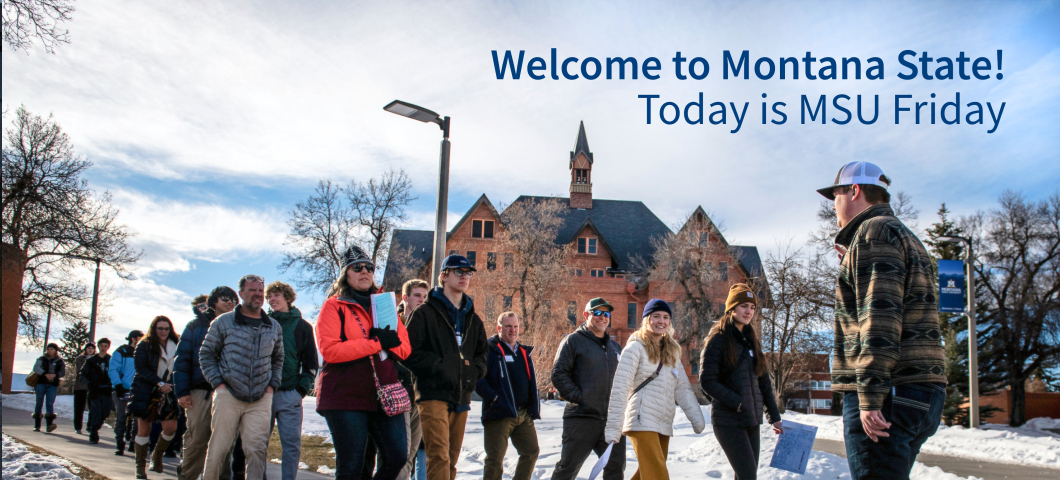 A group of prospective students and their families walk through the snowy Montana State University campus during an MSU Friday event. A student tour guide wearing a patterned jacket and white cap leads the group, gesturing as he speaks. The historic Monta | MSU