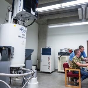 Two people working at a computer in a large room with equipment