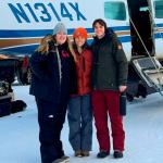 Three people standing next to a small airplane on a snowy tarmac