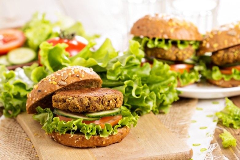 An image of lentil patties on a bun with lettuce, tomatoes, and cucumbers.