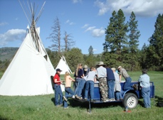 a group of students peer into a truck bed next to two teepees during the River Honoring