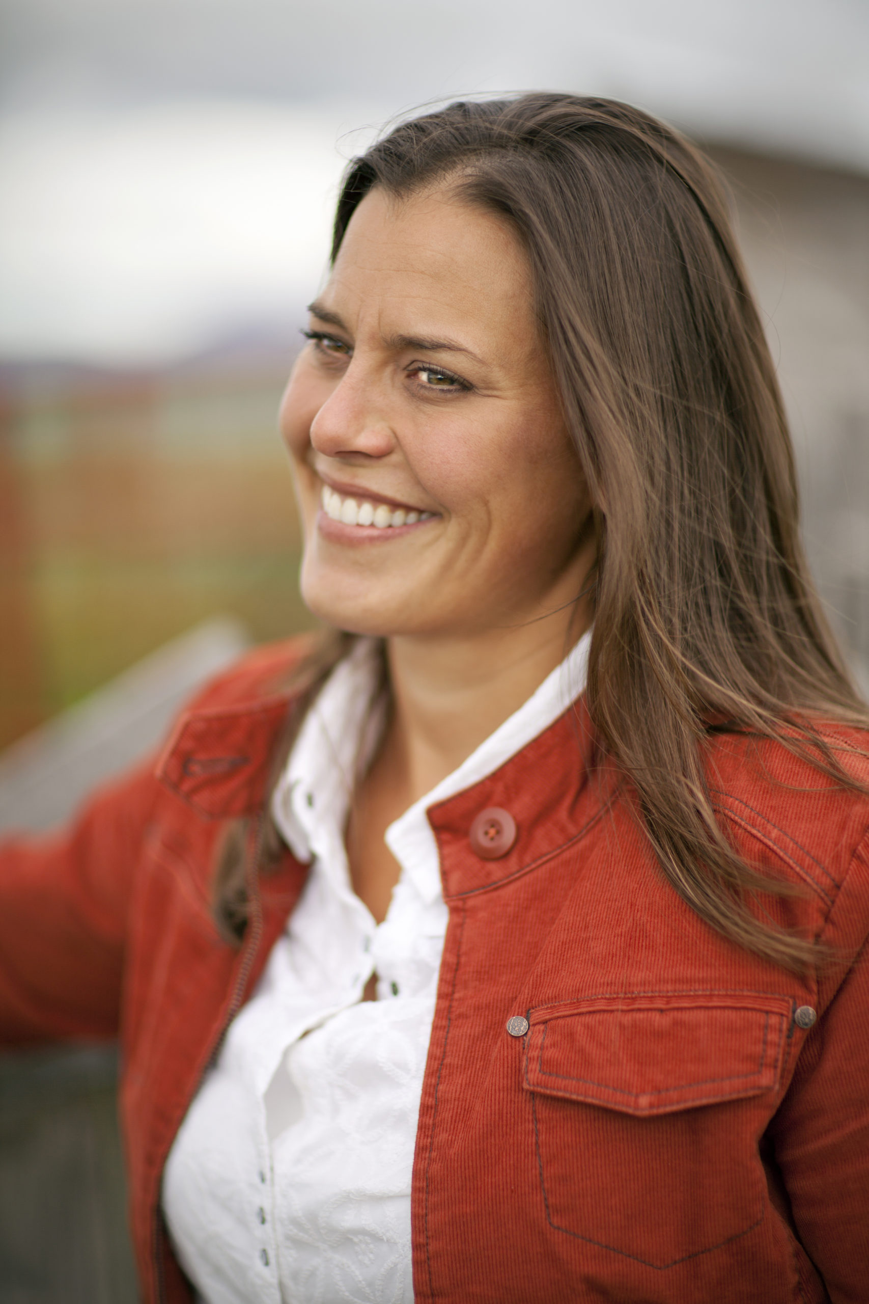 Sarah Calhoun smiling in a red corduroy jacket with a white collared shirt underneath