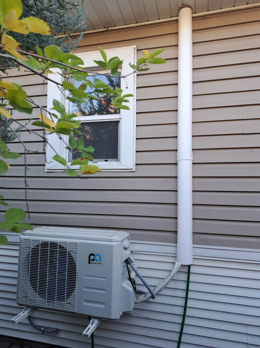 A medium sized grey heat pump that is attached to the side of the house.