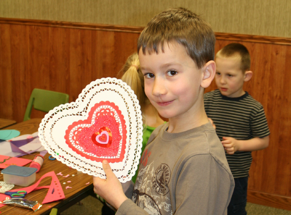 Young boy holding a handmade paper white heart with a red center.