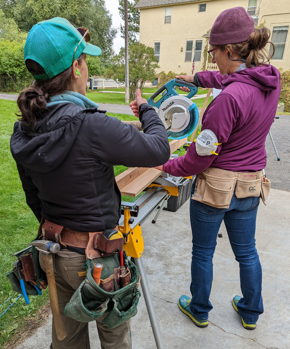 Two women using a circular carpentry saw, one is teaching and the other is learning.