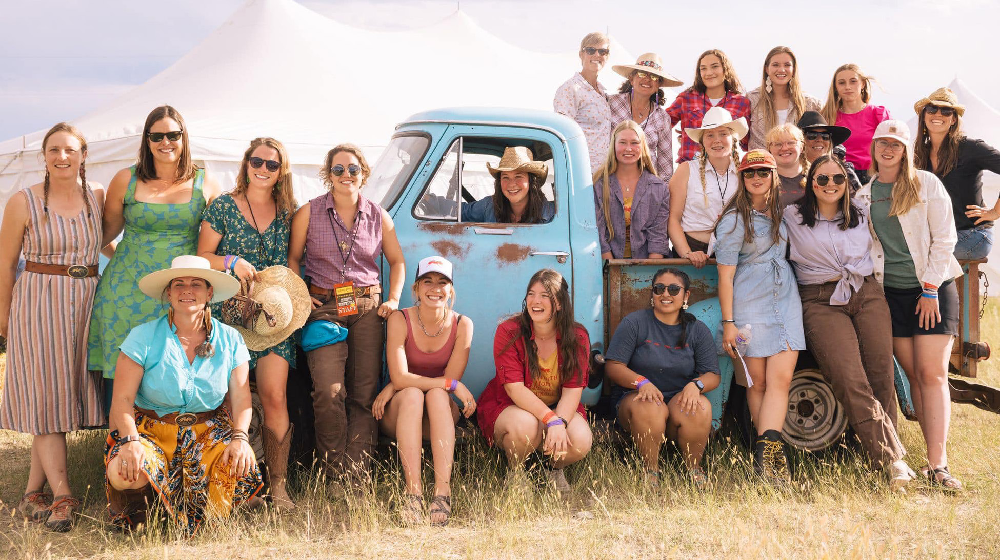 Large group of women surrounding an old blue truck looking happy.