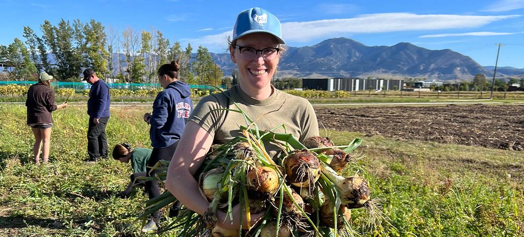 MDI Intern posing with arms full of onions just pulled from the ground at Towne's Harvest Farm