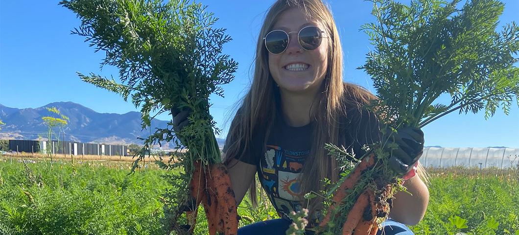 MDI Intern posing with fresh carrots just pulled from the ground at Towne's Harvest Farm