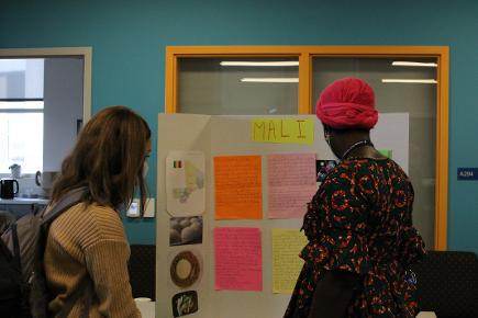 A women in traditional Malian clothing (bright prints and a head scarf) discusses her poster with a young women.