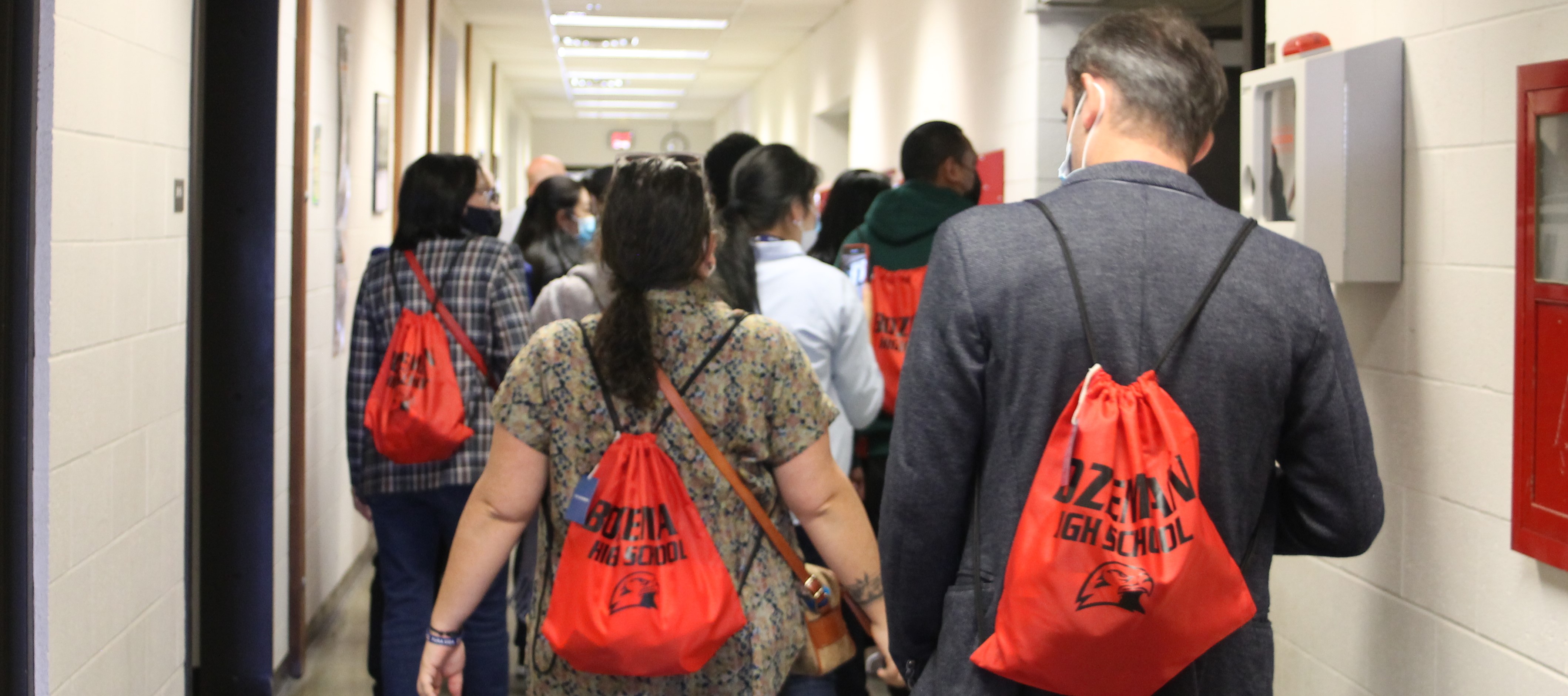 Photo of the backs of several people on a tour, wear Bozeman High School red backpacks.