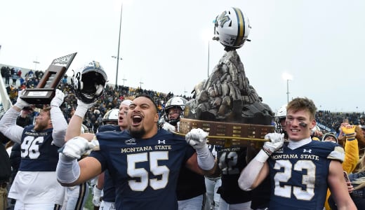 Football players carry a large trophy off the field after a game in celebration.