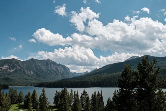 A mountain lake surrounded by tree-covered hills is overset by a partly cloudy sky.