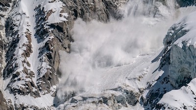 a cloudy wave of snow descends a rocky mountainside